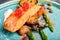 Slice of grilled salmon garnished with cooked green asparagus, sauted cherry tomatoes and lemon