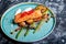 Slice of grilled salmon garnished with cooked green asparagus, sauted cherry tomatoes and lemon