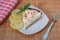 A slice of homemade lemon meringue pie on a plate, with slices of lemons, napkin completing the scene in a rustic setting and