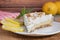 A slice of homemade lemon meringue pie on a plate, with slices of lemons, napkin completing the scene in a rustic setting and