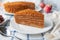 A slice of homemade multilayer honey cake. Orange color. On a white plate. Close-up. Testura. Nearby are berries, apples and cake