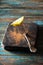 Slice lemon on antique fork on burned-out kitchen board on rough wooden table.