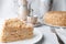 Slice of multilayer Napoleon cake with butter cream. On a white plate. Close-up. Next to a plate is a napkin and a fork. In the