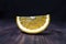 A slice of orange lies on a wooden surface on a dark background