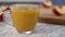 A slice of peach drops in a glass mug with juice on a wooden table with sliced peaches