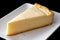 A slice of plain baked cheesecake on white ceramic plate. Black