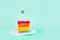 Slice of Rainbow cake with birning candle in the shape of star on white round plate isolated on turquoise background. Happy