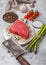 Slice of Raw Beef sirlion steak on round chopping board with tomatoes,garlic and asparagus tips and meat hatchet. Top view