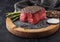 Slice of Raw Beef Topside Joint with Salt and Pepper on stone chopping board with fork and knife, asparagus tips and kitchen towel