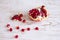 A slice of ripe red pomegranate on a white wooden table and a few pomegranate seeds. Peeled juicy pomegranate