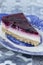 Slice of summer fruit cheesecake with a biscuit base on a blue and white ornate plate.