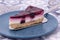 Slice of summer fruit cheesecake with a biscuit base served with a cake cutter utensil on a blue plate.