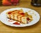 Slice of Tasty Cheesecake with strawberry syrup topping and crumbled cookies on a plate. Closeup view
