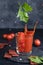 A slice of tomato drops in a glass of tomato juice, spray juice, fresh sliced tomato and bread rolls with tomato on gray