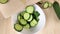 Sliced cucumbers are put in white bowl. Fresh organic green vegetables. Cooking healthy diet food. Close-up, wooden table