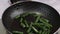 Sliced frozen green string beans fall on a hot frying pan with oil. close-up.