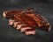 Sliced grilled pork ribs in barbecue sauce on stone surface