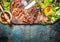 Sliced grilled steak served with green salad, Barbecue sauce and cutlery on wooden gutting board and rustic background, top view