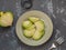 Sliced and half fresh green radish fork and vegetable peeler with wooden handles lay against gray background