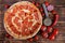 Sliced homemade spicy pizza with pepperoni, salami, red chili peppers, tomatoes and a special circular knife lies on a natural