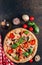 Sliced italian pizza with salami, mozzarella, mushroom, tomatoes, black olives and basil leaves on black background. Italian