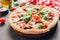 Sliced italian pizza with salami, mozzarella, mushroom, tomatoes, black olives and basil leaves on black background. Italian