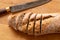 Sliced loaf of whole wheat european bread on light wood next to a rustic bread knife. Top view