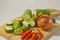 Sliced luffa or gambas or oyong fruit, an onion and some red chilies on a wooden cutting board