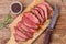 Sliced medium rare roasted beef meat on wooden cutting board, hunters knife