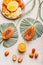 Sliced papaya with seeds on big, green leaves, various halves of orange and yellow fruits on light concrete background. Top view