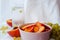 Sliced peaches in bowl, grape and water in glass on white drapery of waffle towel on pink background