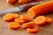 Sliced peeled carrot next to a knife on wood chopping board.