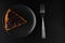 Sliced piece of carrot pie from above covered with currant berries on a black plate and also a table fork on a black background in