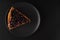 Sliced piece of carrot pie from above thickly covered with currant berries, charlotte on a black plate on a black background on a