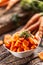 Sliced pieces of carrot in a bowl and a fresh bunch of carrots in the background