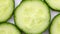 Sliced pieces of green cucumber stacked on a hill rotate clockwise, top view, spinning slowly in a circle, close up.