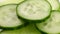 Sliced pieces of green cucumber stacked on a hill rotate counterclockwise, spinning slowly in a circle, close up.