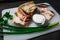 Sliced pieces of lard with layers of meat on a white Board decorated with herbs and salt in a salt shaker.