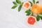 Sliced pink grapefruits and green leaves on white wood board, closeup, border.