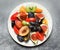 Sliced plums, figs, yellow and red tomatoes, kiwis, grapes on a white porcelain plate, top view.