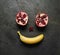 Sliced pomegranate and banana flat-lay in the form of a smile, on dark textured background