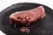 Sliced raw calf meat with a thin layer of fat around it, pink and black peppercorn and sea salt plated on black handmade ceramic