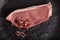 Sliced raw calf meat with a thin layer of fat around it, pink and black peppercorn and sea salt plated on black handmade ceramic