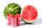 Sliced red watermelon cubes in plastic cup a front of Fresh organic green watermelon and sliced half of watermelon with red