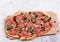 Sliced roman square pizza with cheese, sausage, olives and tomatoes on a round wooden cutting board on a light gray background