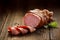 Sliced smoked gammon on a wooden table with addition of fresh herbs and aromatic spices.