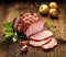 Sliced smoked gammon on a wooden table with addition of fresh herbs and aromatic spices.