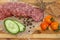 Sliced smoked sausage with bacon and sliced green cucumber and three red tomatoes cherry and pieces of rye bread crumbs