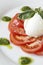 Sliced tomato, mozzarella, pesto and basil leaves on a gourmet plating.