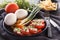 Sliced tomatoes with cheese and herbs in a black plate with onions, sweet peppers, eggs and french fries.